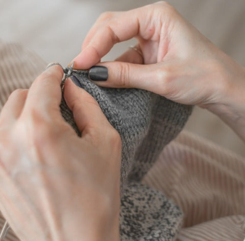 Hands knitting gray yarn on metal needles