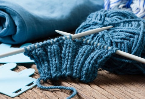 Blue knitted ribbing on white needles beside a ball of yarn